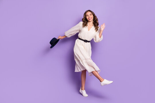 Full length body size photo of dancing in white dress woman holding black hat waving hand isolated on bright purple color background