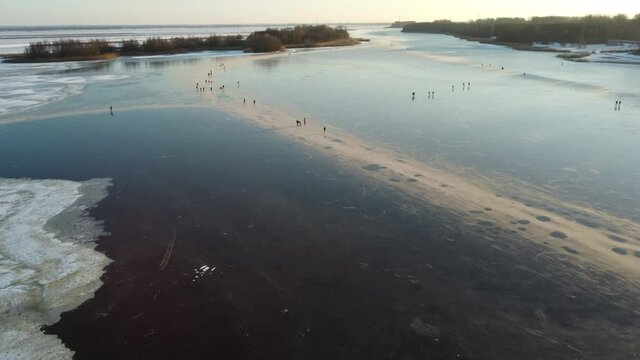 Ice skating people on a frozen lake during a winter sunset in The Netherlands. Aerial drone point of view.