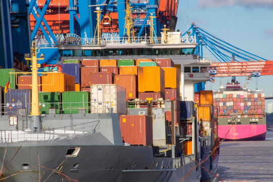 Two container vessels quayside in Harbour during loading at the pier on a sunny day with blue sky and cranes
