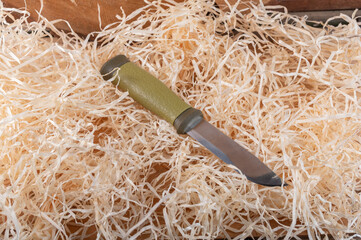 Tourist knife with a fixed blade in the hay. Knife lying in wood shavings.