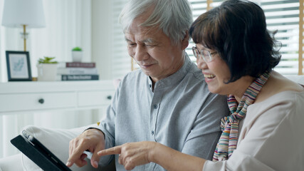 Obraz premium Candid old asian retired couple use tablet computer to transfer money online or financial payment and read text, smile or laugh with happy and positive. Senior asia with digital technology concept.