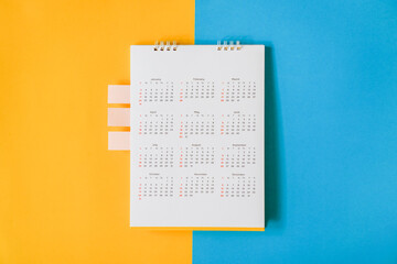 top view of white yearly calendar with small pink tag on grunge yellow and blue paper background