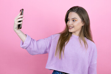 Naklejka premium Young pretty woman with long hair standing over isolated pink background smiling and taking a selfie with her phone