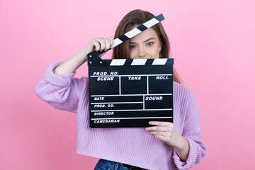Young pretty woman with long hair standing over isolated pink background holding clapperboard very...