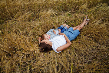 Naklejka na ściany i meble Happy family of mother and son in a wheat field. They lie and rest in nature. Summer rural landscape.