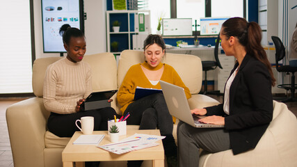 Friendly creative diverse colleagues team discussing about online project using laptop and tablet at workplace. Multiracial coworkers group working together sharing marketing ideas at office meeting