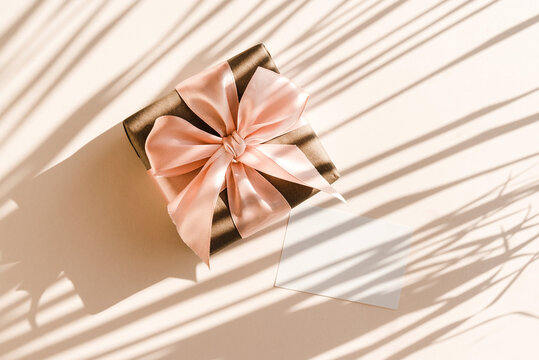 Blank card and gift box on beige background with shadows shape palm leaves. Minimal concept.