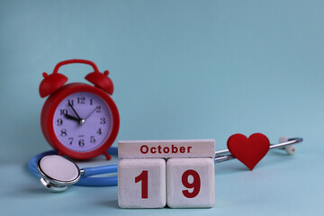 October 19. Day of the 19th month, calendar date. White wooden calendar blocks with date, clock and stethoscope on blue pastel background. Selective focus. health concept