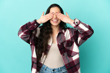 Young caucasian woman isolated on blue background covering eyes by hands and smiling