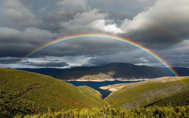 Rainbow in the dam with dark clouds, light rain and second rainbow