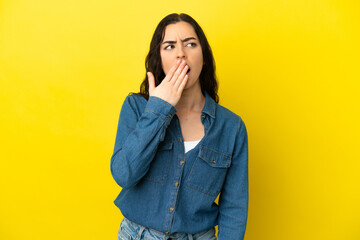 Young caucasian woman isolated on yellow background yawning and covering wide open mouth with hand