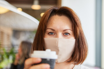 Frau mit Mundschutz sitzt mit Kaffeebecher im Cafe