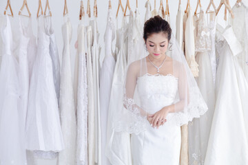 Beautiful Asian bride happy post to camera while dress up elegant wedding lace dress, wedding dress maker try to fit the bride suit in wedding studio or Wedding dress shop store