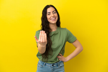 Young caucasian woman isolated on yellow background inviting to come with hand. Happy that you came