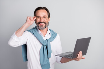 Portrait of positive guy hand touch eyewear hold netbook tied on shoulders sweater isolated on grey color background