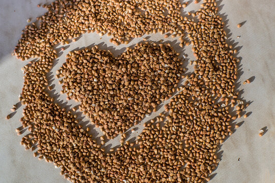 Heart shape made from buckwheat grains. Rural still-life - the peeled groats of buckwheat (Fagopyrum esculentum) on the background © Viktoryia Kam