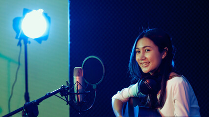 A cute Asian singer and musician playing guitar and sing a song for recording in voice studio.