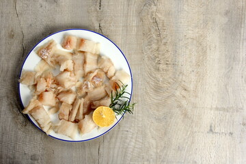 Pieced of sea fish filet on a white plate decorated with lemon and rosemary, white raw fish on a...