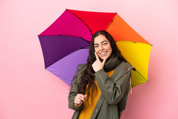 Young woman holding an umbrella isolated on pink background happy and smiling