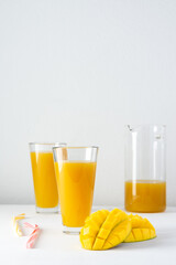 Mango juice in a glass jug and glasses with juice and a straw on a white background, chopped mango and whole, delicious healthy sweet natural drink