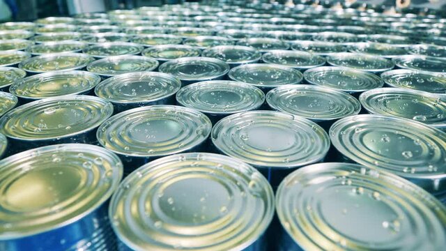 Sealed tin cans are getting stocked together. Food factory conveyor, automation concept.