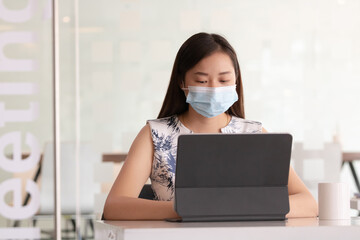 Asian woman wearing medical mask and working with digital tablet or laptop computer.