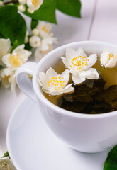 Close-up cup of green tea with white jasmine flowers on white background