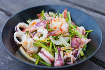 Spicy salad with shrimp and squid was mixed with chopped tomato and onion on the black dish.