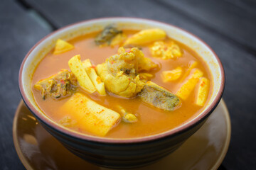 Spicy sour yellow curry with  coconut shoots and sea fish is one of Southern of Thai food on wood table as a background.