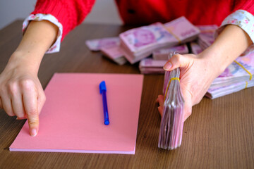 An agreement between woman and client. Lady waiting her client to sign on pink paper. Adult lady...