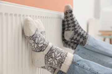 Couple warming legs on heating radiator indoors, closeup