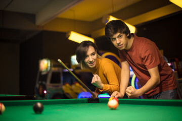 Young couple spending time in billiard room. Woman is a winner.