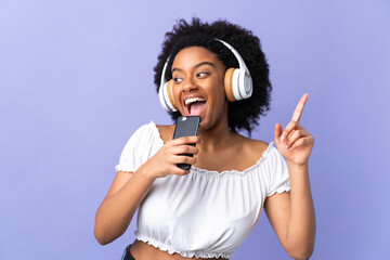Young African American woman isolated on purple background listening music with a mobile and singing