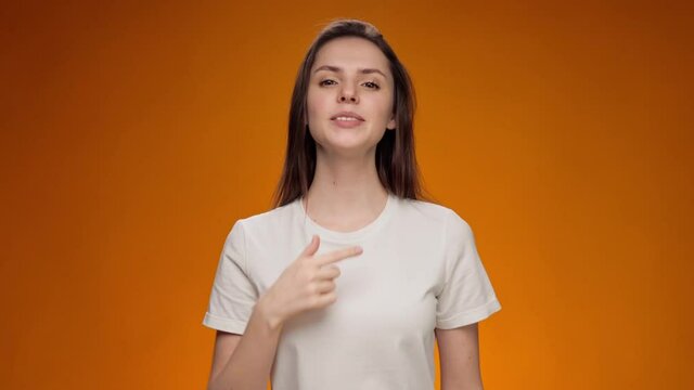 Friendly young woman communicating with deaf-mute sign language against yellow background
