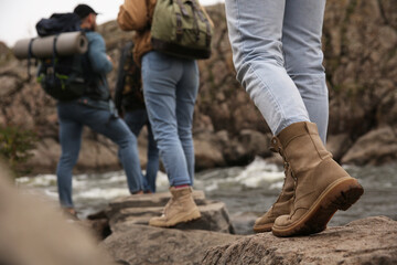 Group of friends with backpacks crossing mountain river, focus on hiking boots