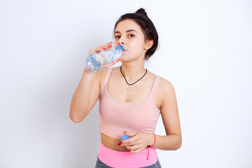 Naklejka premium Brunette girl drinks water in sports uniform after training. White background. Portrait. Health