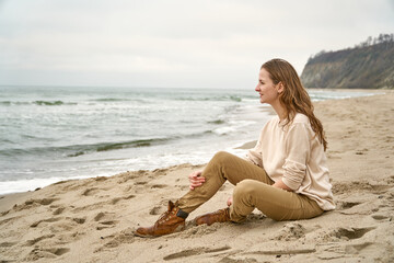 Fototapeta na wymiar Girl on the beach have fun. Caucasian beautiful woman is happy on the beach against the background of the sea. Beige clothes and sand in the fall. High quality photo