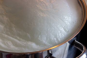 Close up view of floating cream on the boiling milk in the steel pot. Selective focus.