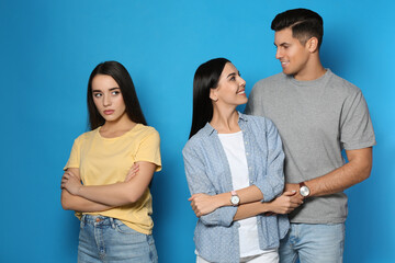 Unhappy woman feeling jealous while couple spending time together on blue background