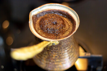 Close-up view of Turkish coffee cooked on the stove in a copper coffee pot. Selective focus.