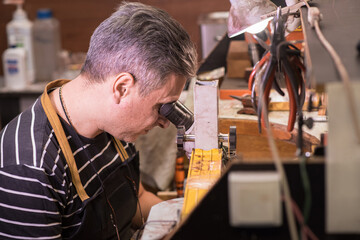 A male jeweler looks through a microscope and fixes a gem on a pendant