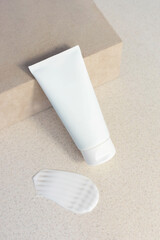 white cosmetic tube with face or hand cream, cleanser or body lotion on a beige sand background with cream swatch leaning against a suede box. Gentle skin care concept. Vertical