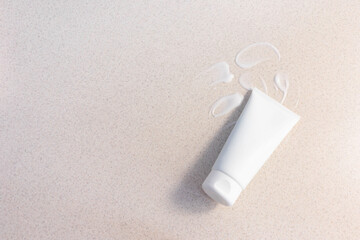 white cosmetic tube on a light sand background with cream smears. Copy space

