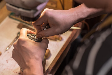 A male jeweler fixes precious stones on a silver pendant