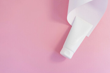 white cosmetic tube for face cream, hand, body lotion or cleanser on pink background with white paper sheet. Copy space