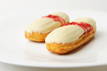 French dessert eclair with vanilla cream and strawberry sauce on white plate. Elegant serving style