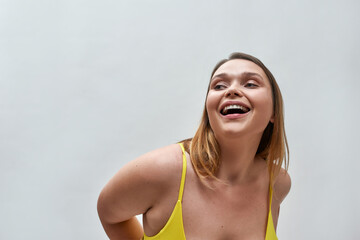 Portrait of happy young woman wearing yellow bra posing isolated over grey background