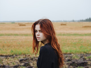 Portrait of a red-haired woman in a black dress in a field in nature cropped view