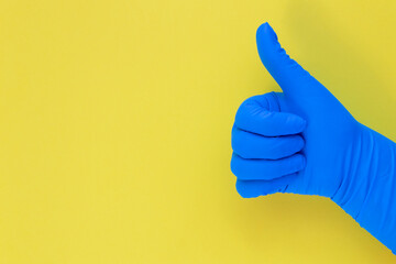View of doctor's hand with thumb up in blue medical (surgical) gloves an yellow background. Banner size with space for text.