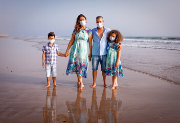 Family on the beach. Summer holidays during a pandemic covid-19. A family of 4 people, mother, father, son and daughter walk along the shore in protective masks. Agadir Morocco.